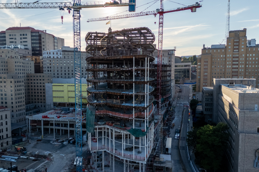 Tall building being built in the city with two cranes on each side.